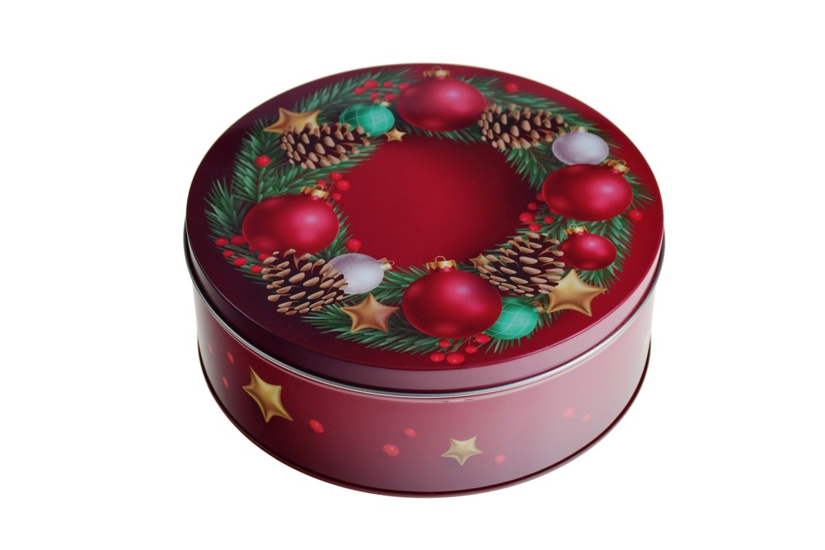 Geschlossene runde Blechdose mit weihnachtlichem Motiv, roter Hintergrund mit Tannenzweigen, Zapfen, goldenen Sternen und roten Kugeln, auf neutralem Hintergrund fotografiert.