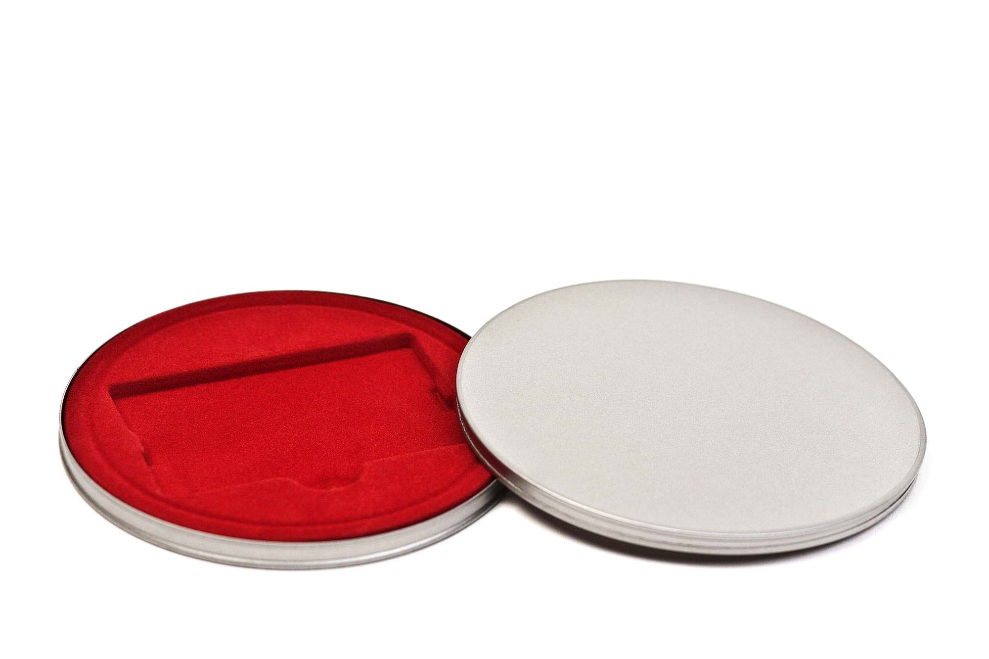 Geöffnete runde Metalldose aus silberfarbenem Metall mit rotem Samteinsatz, auf weißem Hintergrund fotografiert.