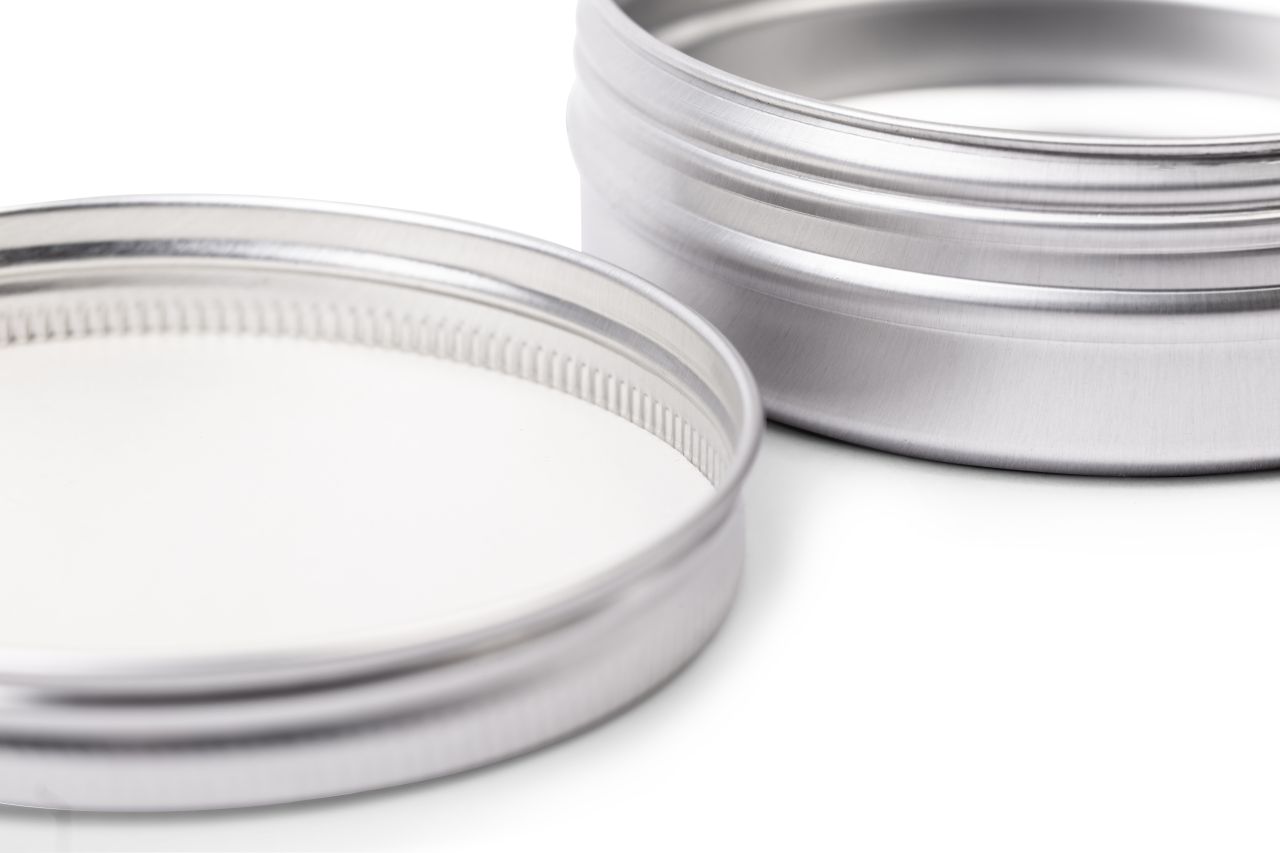 Nahaufnahme einer geöffneten silbernen Aluminiumdose mit 125 ml Volumen. Der Fokus liegt auf dem Schraubgewinde und der Innenseite des Deckels, die eine weiße Creme zeigt.