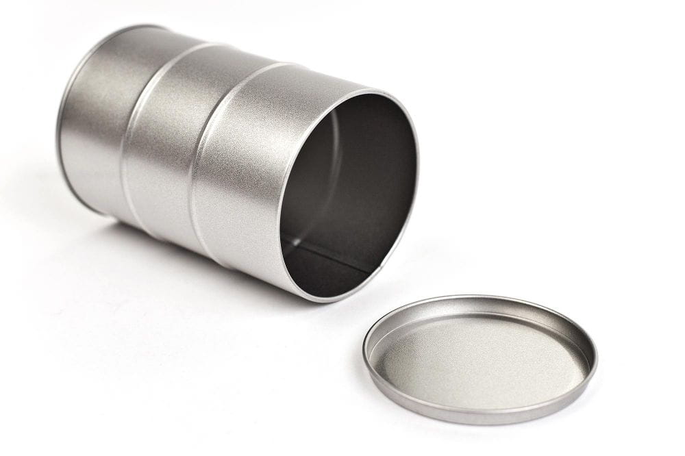 Geöffnete runde Metalldose in Form eines Ölfasses, silberfarben, liegend mit abgenommenem Stülpdeckel, auf weißem Hintergrund fotografiert.