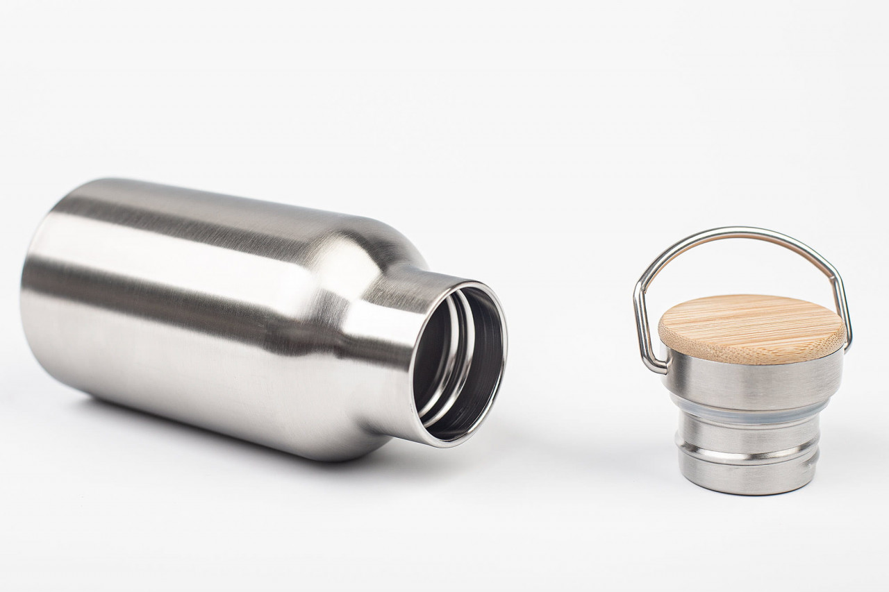 Geöffnete Edelstahl-Trinkflasche mit abgenommenem Schraubdeckel, Deckel mit Bambuseinsatz und Metallbügelgriff, auf weißem Hintergrund fotografiert.