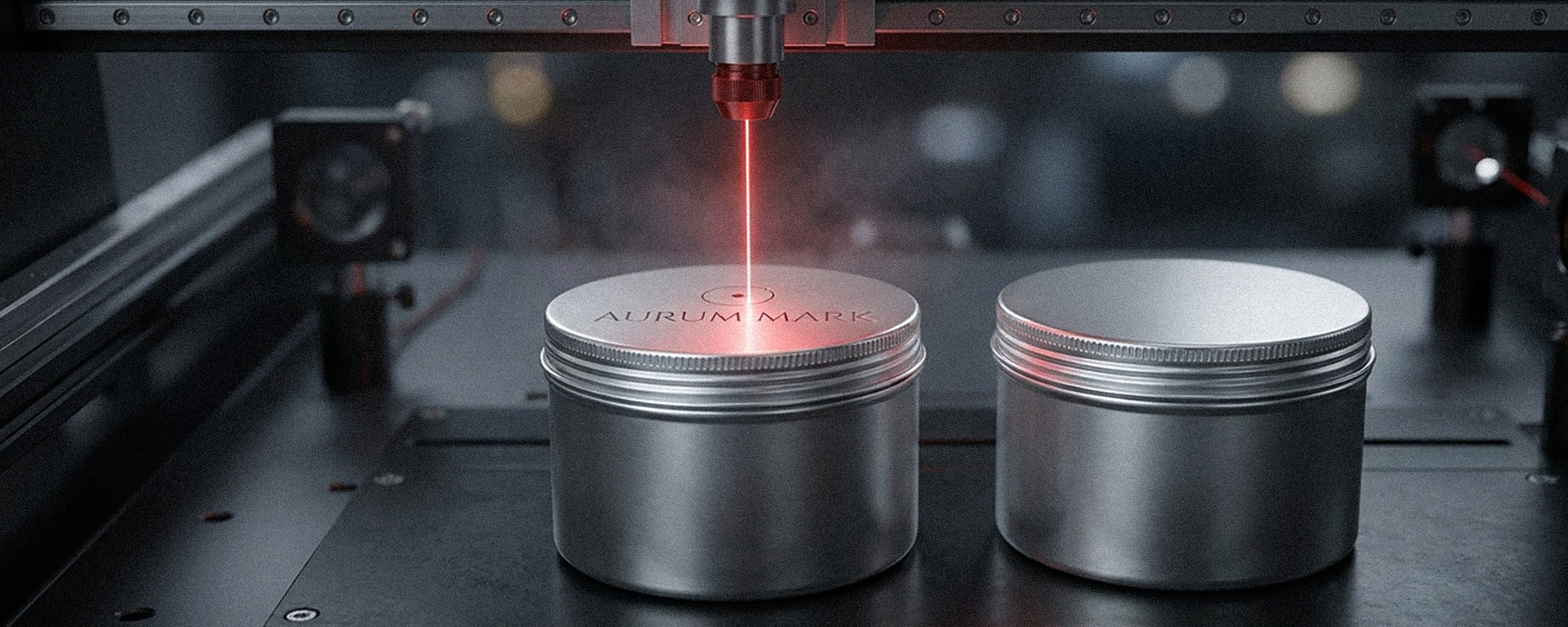 Laserbeschriftung von zwei zylindrischen Metalldosen in einer Industrieanlage; ein roter Laser graviert „AURUM MARK“ auf den Deckel, während Rauch und Präzisionsmaschine sichtbar sind.